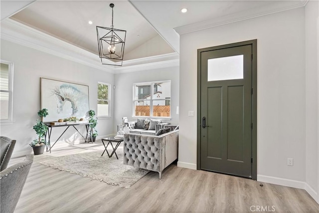 foyer with a tray ceiling, crown molding, an inviting chandelier, and light wood-type flooring