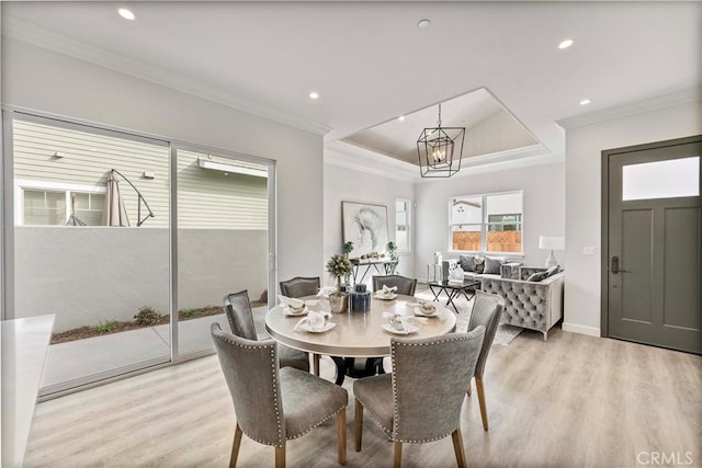 dining room with ornamental molding, an inviting chandelier, light wood-type flooring, and a tray ceiling