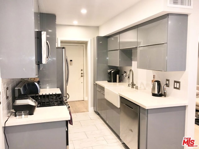 kitchen featuring sink, backsplash, gray cabinetry, and stainless steel appliances