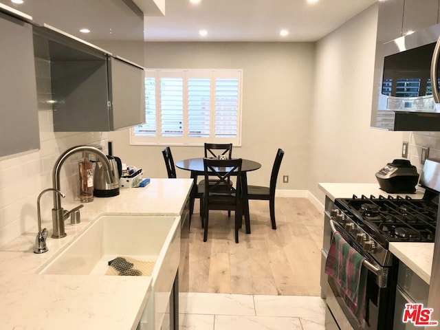 kitchen featuring light stone countertops, stainless steel appliances, tasteful backsplash, sink, and gray cabinets