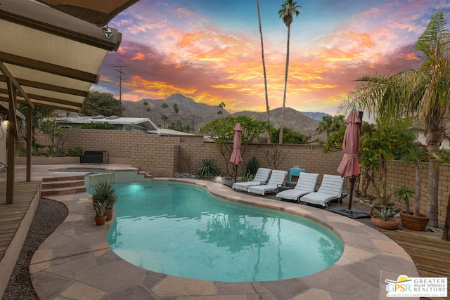 pool at dusk featuring a patio area, a mountain view, and an in ground hot tub