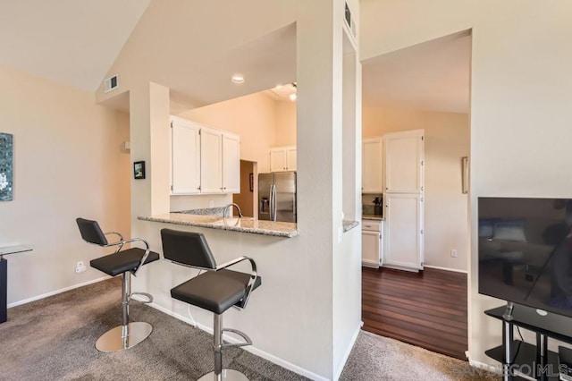 kitchen featuring white cabinetry, light stone counters, vaulted ceiling, stainless steel fridge with ice dispenser, and kitchen peninsula