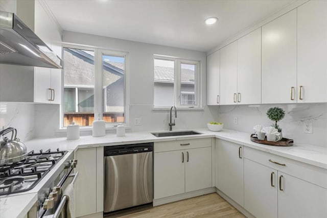 kitchen featuring stainless steel appliances, wall chimney exhaust hood, white cabinetry, and sink