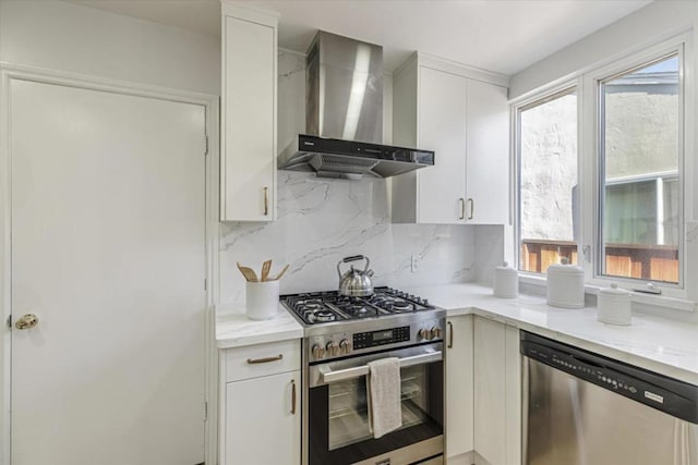 kitchen featuring white cabinetry, appliances with stainless steel finishes, decorative backsplash, wall chimney range hood, and light stone counters