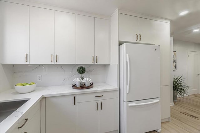 kitchen featuring light stone countertops, white cabinets, white refrigerator, and light hardwood / wood-style flooring