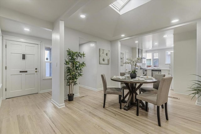 dining area with lofted ceiling with skylight and light hardwood / wood-style floors