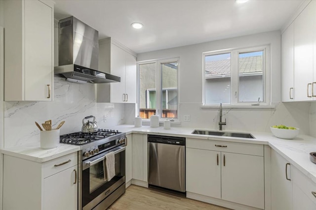 kitchen featuring appliances with stainless steel finishes, white cabinetry, wall chimney range hood, decorative backsplash, and sink