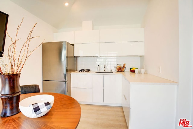 kitchen featuring stainless steel refrigerator, white cabinetry, sink, backsplash, and gas cooktop