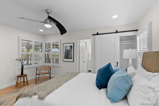 bedroom featuring ceiling fan, wood-type flooring, ensuite bathroom, and a barn door