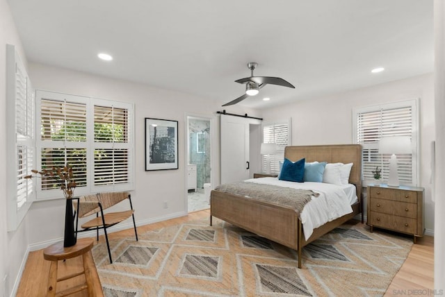 bedroom with ceiling fan, light hardwood / wood-style floors, ensuite bath, and a barn door