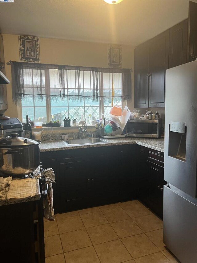 kitchen with light stone countertops, light tile patterned floors, appliances with stainless steel finishes, and sink