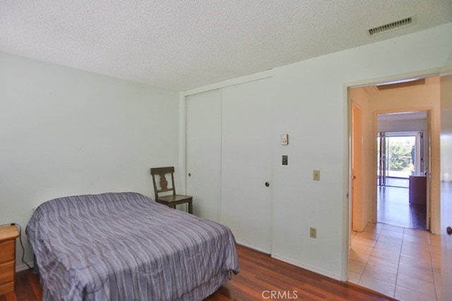 bedroom featuring a textured ceiling, wood finished floors, visible vents, baseboards, and a closet