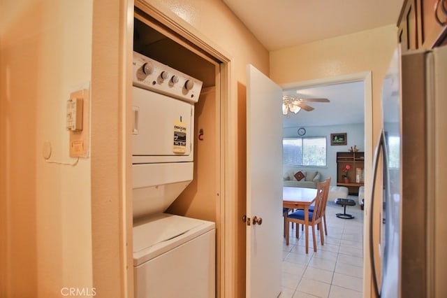 clothes washing area featuring stacked washer and dryer, laundry area, light tile patterned flooring, and ceiling fan