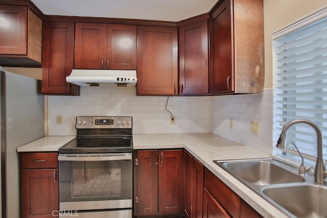 kitchen with light stone counters, under cabinet range hood, a sink, appliances with stainless steel finishes, and tasteful backsplash