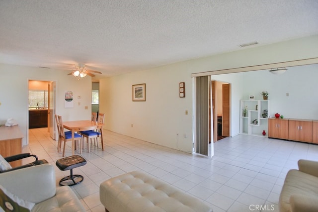 living area with a textured ceiling, light tile patterned floors, visible vents, and a ceiling fan