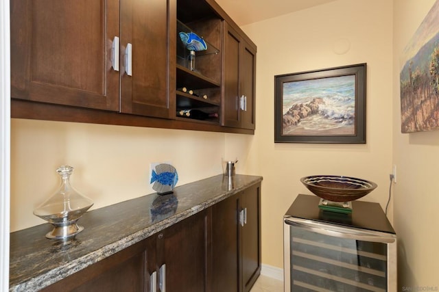 bar featuring beverage cooler, dark brown cabinets, and dark stone countertops