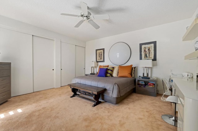 bedroom with multiple closets, light colored carpet, a textured ceiling, and ceiling fan