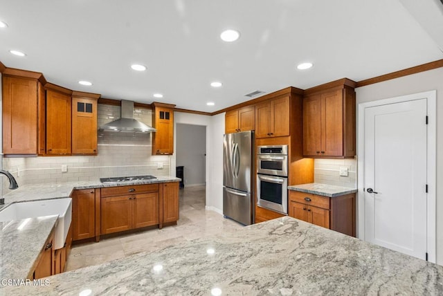 kitchen featuring light stone countertops, appliances with stainless steel finishes, wall chimney exhaust hood, sink, and backsplash