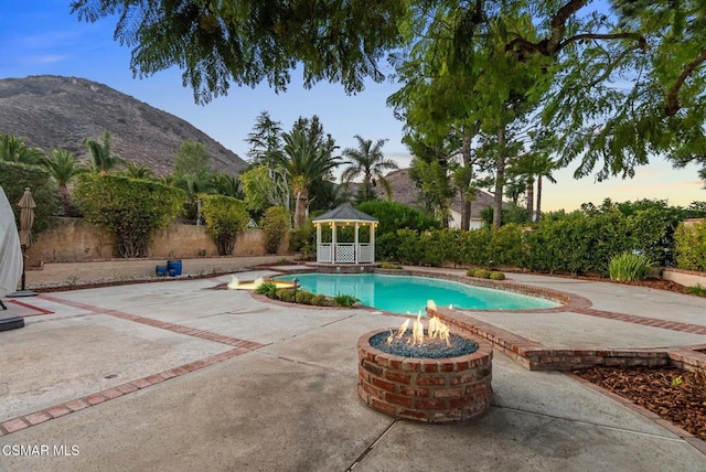 pool at dusk with a mountain view, a gazebo, and an outdoor fire pit