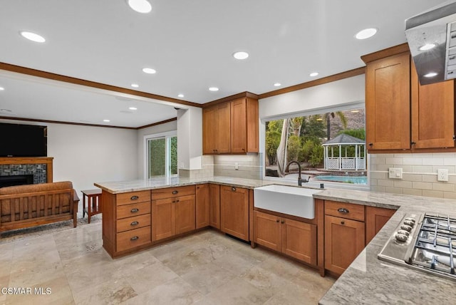 kitchen featuring kitchen peninsula, sink, stainless steel gas cooktop, a stone fireplace, and ornamental molding