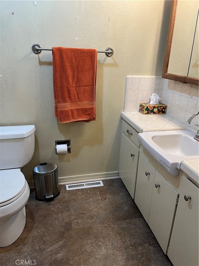 bathroom with toilet, vanity, and tasteful backsplash