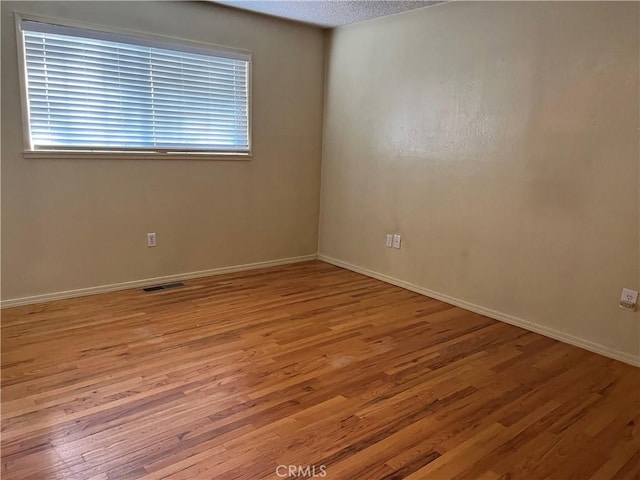 empty room with a textured ceiling and light hardwood / wood-style flooring