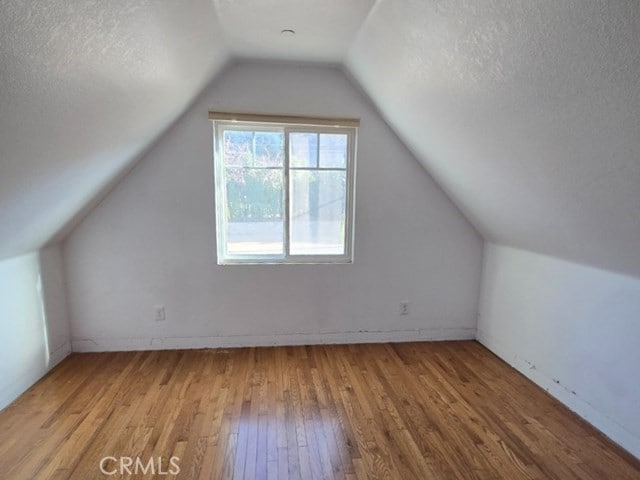 additional living space with a textured ceiling, lofted ceiling, and light hardwood / wood-style flooring