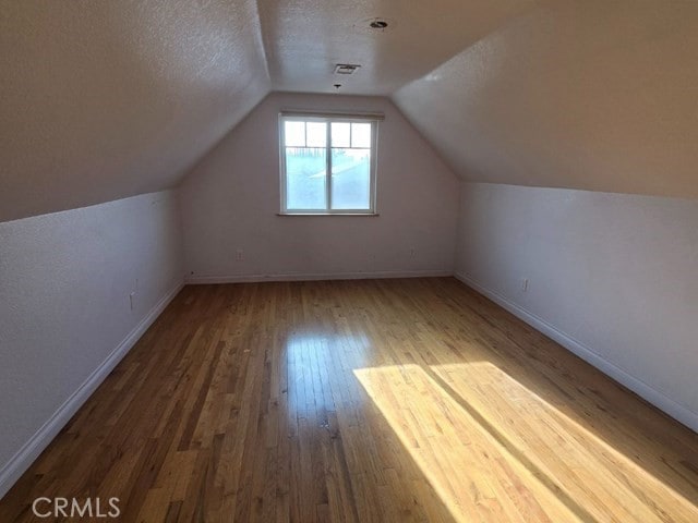 additional living space featuring a textured ceiling, vaulted ceiling, and wood-type flooring