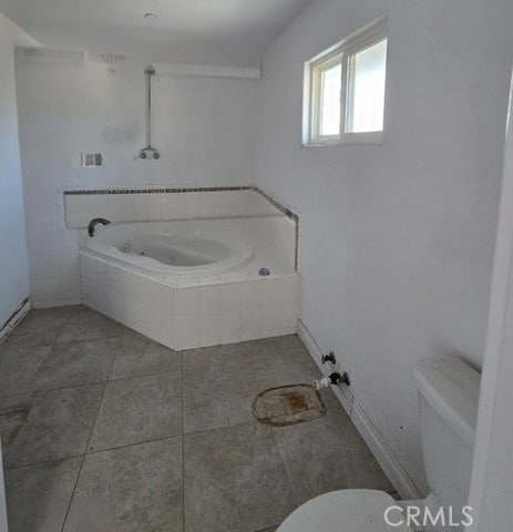 bathroom featuring toilet, tile patterned flooring, and a relaxing tiled tub