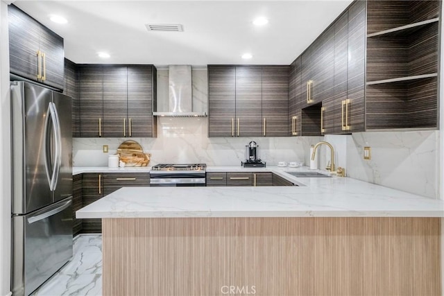 kitchen with appliances with stainless steel finishes, wall chimney range hood, decorative backsplash, sink, and light stone counters