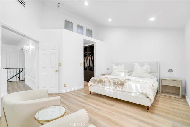 bedroom with a walk in closet, light wood-type flooring, a notable chandelier, and a closet