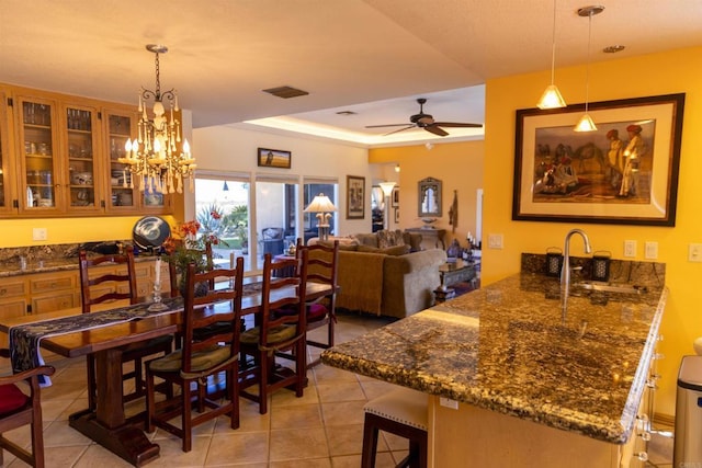 tiled dining room featuring ceiling fan with notable chandelier, a tray ceiling, and sink