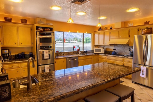 kitchen with stainless steel appliances, dark stone countertops, hanging light fixtures, a breakfast bar, and sink