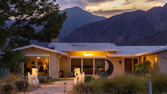 back house at dusk with a mountain view and a patio