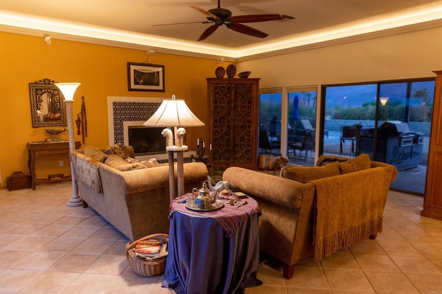 living room featuring ceiling fan, light tile patterned flooring, a tile fireplace, and a tray ceiling