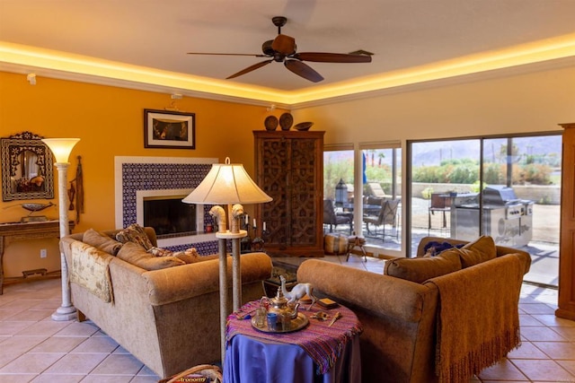 living room with ceiling fan, light tile patterned flooring, a tray ceiling, and a tile fireplace