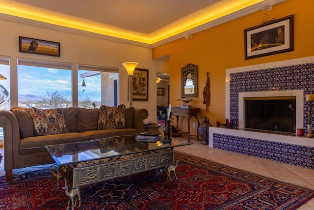 tiled living room with a tray ceiling, a tile fireplace, and crown molding