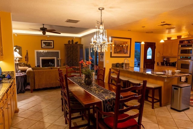 tiled dining room featuring ceiling fan with notable chandelier and a fireplace