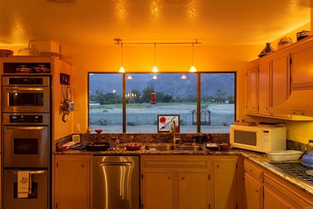 kitchen featuring stainless steel double oven, sink, dark stone countertops, and pendant lighting