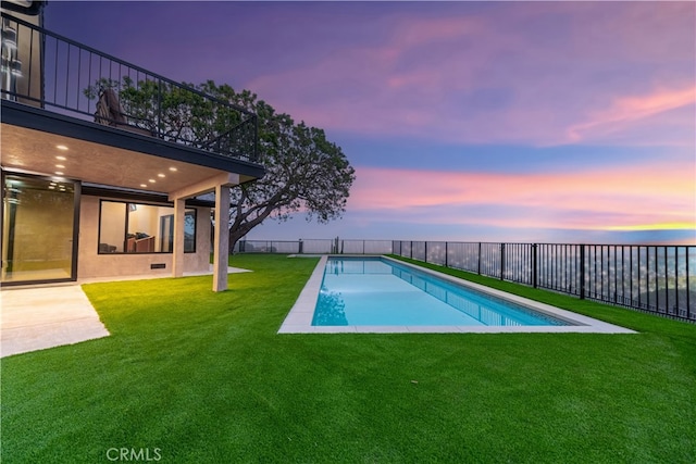 pool at dusk with a patio area and a yard