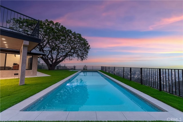 pool at dusk featuring a lawn