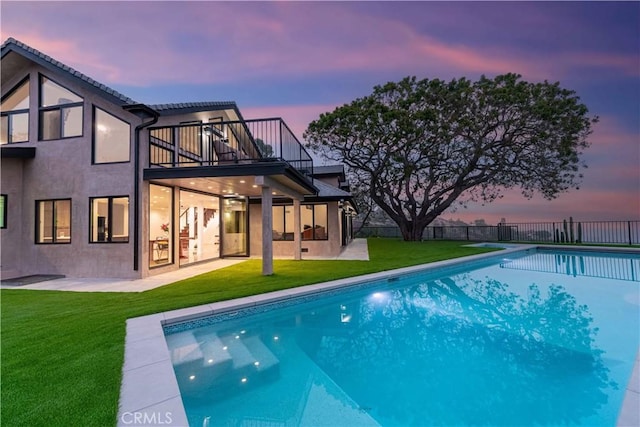 back house at dusk with a yard, a patio area, a fenced in pool, and a balcony