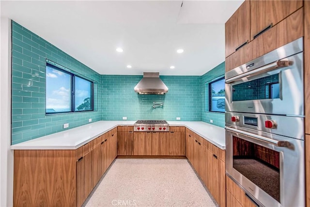 kitchen with backsplash, appliances with stainless steel finishes, and wall chimney exhaust hood