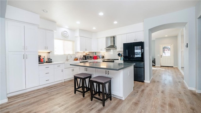 kitchen featuring a center island, wall chimney exhaust hood, white cabinetry, and black fridge