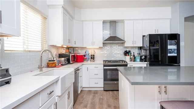 kitchen with stainless steel appliances, decorative backsplash, white cabinets, wall chimney exhaust hood, and light hardwood / wood-style flooring