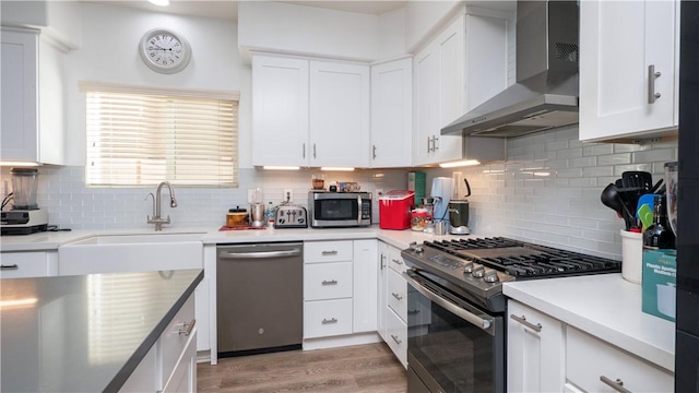 kitchen featuring white cabinets, wall chimney range hood, stainless steel appliances, decorative backsplash, and sink