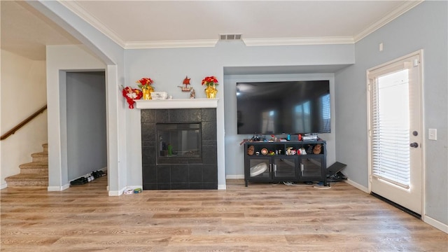 living room featuring a tile fireplace, crown molding, and light hardwood / wood-style floors