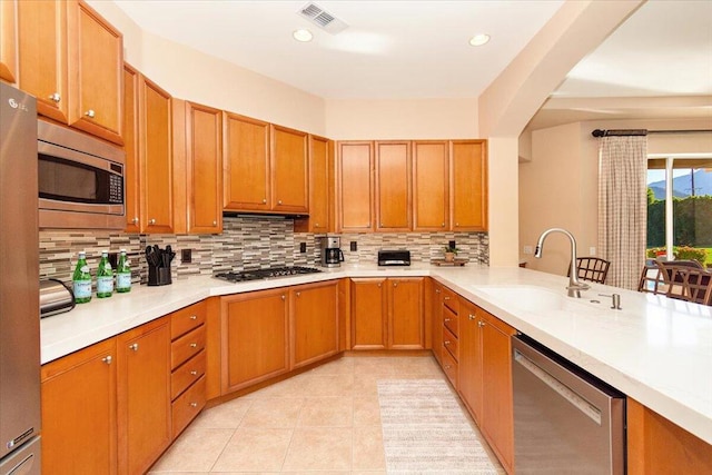 kitchen featuring backsplash, kitchen peninsula, sink, stainless steel appliances, and light tile patterned floors