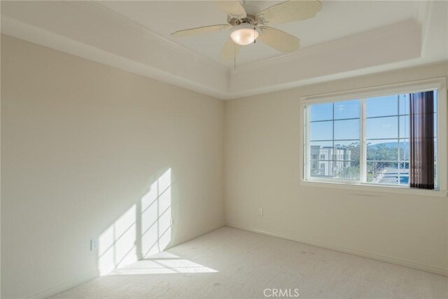 carpeted spare room with ornamental molding, a tray ceiling, ceiling fan, and baseboards