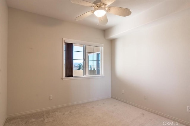 empty room with baseboards, a ceiling fan, and light colored carpet